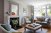 Two seater sofa in bay window with mirror above fireplace and ottoman in Surrey cottage UK