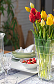 Rote und gelbe Tulpen in einer Glasvase mit Erdbeeren auf einem Tisch in einem Londoner Haus UK