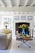 Cut flowers on coffee table with sofa in whitewashed living room of Surrey cottage UK