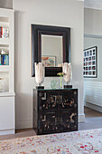 Black lacquered cabinet with matching lamps and mirror in London hallway UK