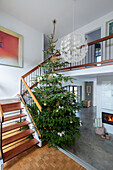 Doppelt hohe Eingangstreppe mit großem Weihnachtsbaum und Zementboden in einem Landhaus aus den 1960er Jahren in West Sussex, Großbritannien