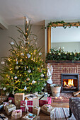 Weihnachtsgeschenke unter dem Baum mit beleuchtetem Feuer in einem Cottage in Hampshire UK