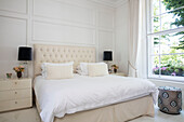 Bedroom in gentle creams and whites with peacock footstool London townhouse UK