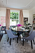 Graue Esszimmerstühle am ovalen Tisch mit goldenen Vorhängen in einem Londoner Stadthaus UK
