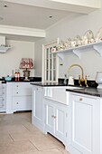 Weiße und hellblaue Küche mit dunkelgrauer Arbeitsplatte und offenen Regalen mit altem Porzellan in einem eleganten Haus in Hampshire, Großbritannien