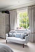 Elegant master bedroom with pale blue botanical patterned wallpaper and bed filled with pillows and cushions in Hampshire UK