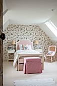 Schlafzimmer im Dachgeschoss mit hübscher Blumentapete und Einzelbett mit rosa Kopfteil in Hampshire, Großbritannien