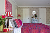 Kantha bedspread with striped lamps on side tables and floral wallpaper in Hampshire home UK