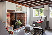 Light grey armchair and footstool with woodburner in exposed brick fireplace Surrey UK