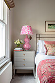 Pink lamp on grey bedside cabinet London UK