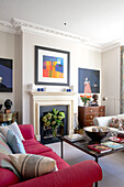 Moderne Kunst und rosa Sofa im Wohnzimmer eines Hauses im Südwesten Londons UK