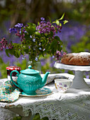 Türkisfarbene Teekanne und Kuchen mit Schnittblumen auf Tisch in Bluebell Woods
