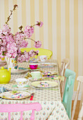 Rosa Blüte und gedeckter Tisch für den Nachmittagstee in einem Zimmer mit gestreifter Tapete