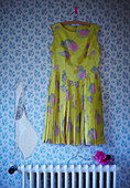 Vintage Blooms - Yellow floral dress handing against torn wallpaper above a radiator with a pink cup and head of a hydrangea