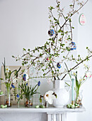 Zweig mit weißer Blüte und bemalten Eiern in einer Vase auf dem Kaminsims mit anderen Frühlingsblumen