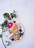 Overhead view of plate on table top with Holly baubles and a gift with label 'Merry Christmas' and a mince pie