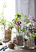Herstellung von Blumenschmuck für einen Ostertisch Glasgefäße und Vasen mit Karten, die mit Schnur gebunden und mit Frühlingsblumen gefüllt sind, neben dem Fenster