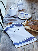 Linen bread bag on wooden table top with enamelware teapot and mug