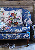 Sofa mit blauem, geblümtem Stoff bezogen, mit geblümten Kissen und Plimpsolen