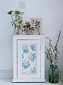 White cabinet with floral wallpaper insert with botanical prints and fresh flowers in glass vases