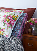 Vintage-Bettwäsche mit spitzenbesetzten Kissen und Vase mit frischen Blumen auf dem Nachttisch