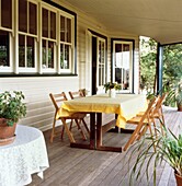 Holzgetäfeltes Haus im kolonialen Landhausstil mit großer Veranda und Esstisch und zusammenklappbaren Gartenstühlen aus Segeltuch