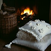Pile of neutral embroidered cushions in front of a lit log fire in a living room
