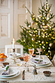 Festlich gedeckter Tisch im Esszimmer mit geschmücktem Weihnachtsbaum und brennenden Kerzen