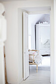 Blick durch die Schlafzimmertür auf einen weiß gestrichenen, verspiegelten Kleiderschrank und einen alten Stuhl auf gestrichenen Dielen