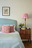 Double bed with pillows and antique bedside cabinet with lamp in bedroom