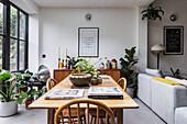 Bright dining area with wooden table and plants next to windows