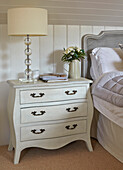 White chest of drawers with lamp next to rattan headboard in bedroom