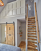 Wooden staircase to a gallery in a bedroom with a rustic sliding door