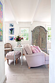 Living room with pink sofa, antique wardrobe and floral decorations