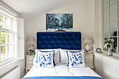 Bedroom with blue velvet headboard and white cushions with blue floral pattern