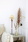 Vases with grasses and lamp on side table in white corner of room