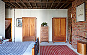 Double bed and wooden armoires in bedroom with brick wall