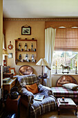 Armchair with tartan throw below collection of historical soldier figurines on wooden shelves