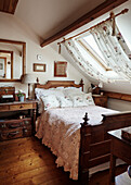 Antikes Holzbett mit nostalgischer Bettwäsche und Tagesdecke im Dachzimmer