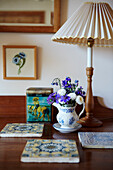 Tiles as table set on wooden table, jug with bouquet of flowers and table lamp