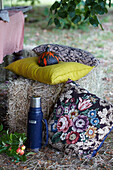 Straw bales as seating with colourful cushions and thermos flask in the garden