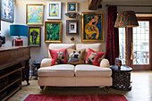 Cushions with dog motifs on cosy two-seater in front of gallery of pictures in rustic room