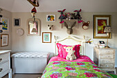Wooden bed with colourful blanket, sitting chest and stuffed animals in a rural children's room