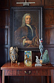 Antique table with sculptures, and a portrait painting hung above it