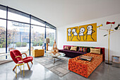Bunte Sitzmöbel und abstrakte Kunst an weißer Wand im Wohnzimmer mit Glaswand