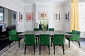 Large table with green upholstered chairs in elegant room with gallery of pictures