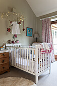 White cot below fairy lights in baby girl's bedroom