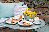 Gebäck, Kaffee und herbstliches Blumenarrangement auf Bistrotisch im Freien