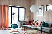 Living room with wooden wall paneling, designer rocking chair and colorful cushions on a grey corner sofa