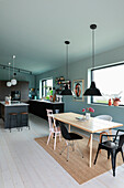 Open-plan kitchen and dining area with black kitchen and light-colored wooden table with chairs